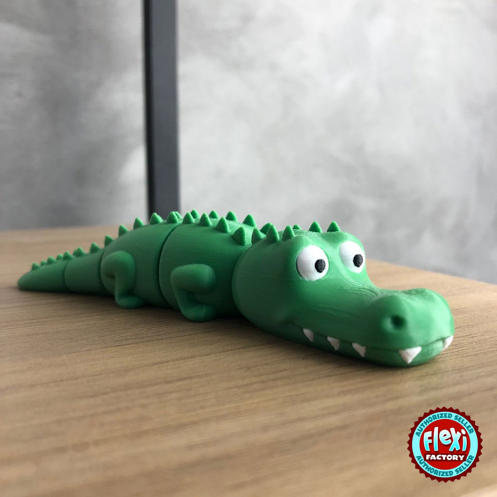 Cute crocodile keychain, 3D printed by RU3D – on wooden table. Green with white teeth.