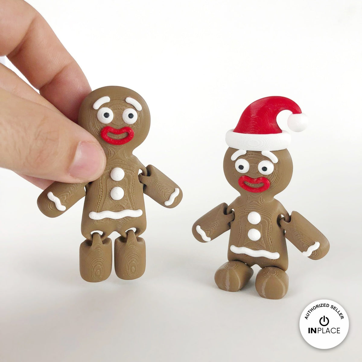 Cute gingerbread man keychain, 3D printed by RU3D – held in hand next to Santa hat version. Brown with white icing and red Santa hat.