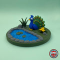 Cute peacock keychain, 3D printed by RU3D – three quarter view with pond garden. Royal blue with green feather tail and pond garden playset.