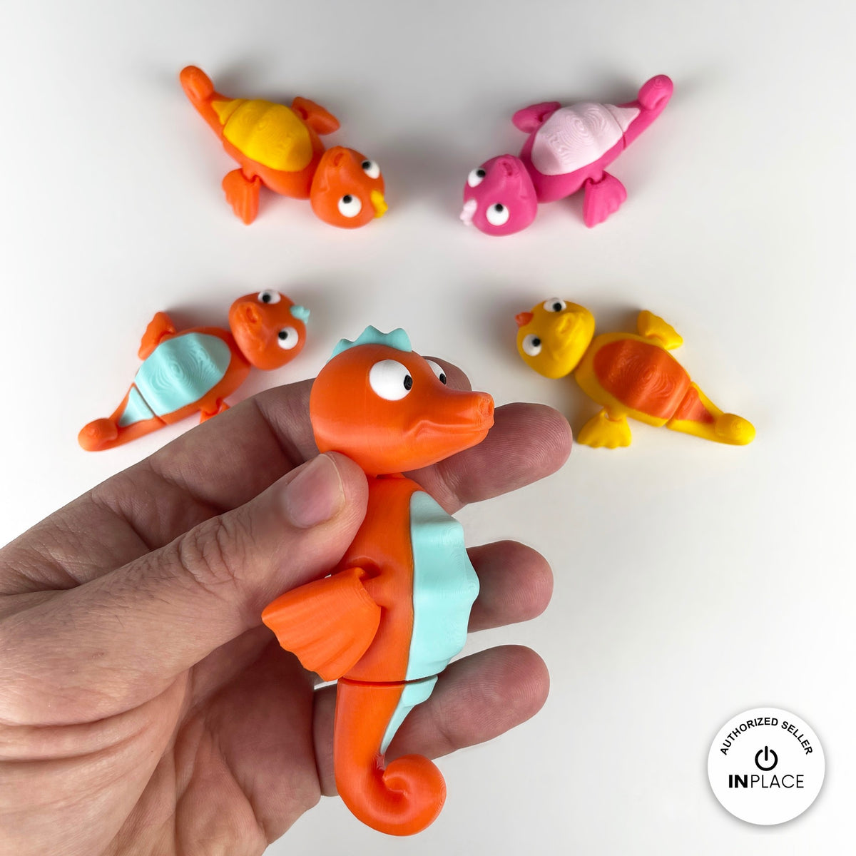 Cute seahorse keychain, 3D printed by RU3D – held in hand with friends. Orange with mint belly, also pink and yellow.