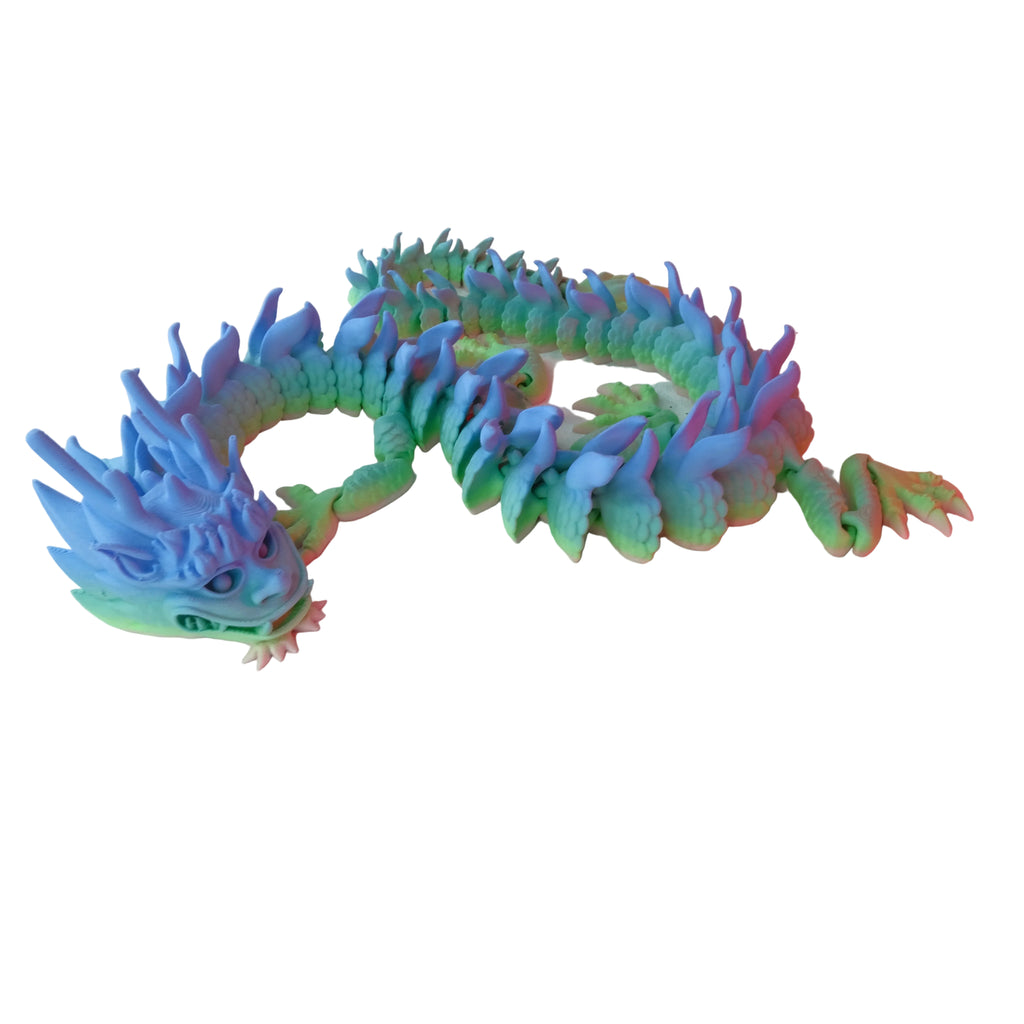 A multicoloured dragon figurine with spikes and a long body, featuring shades of green and blue, resting directly on a white surface.