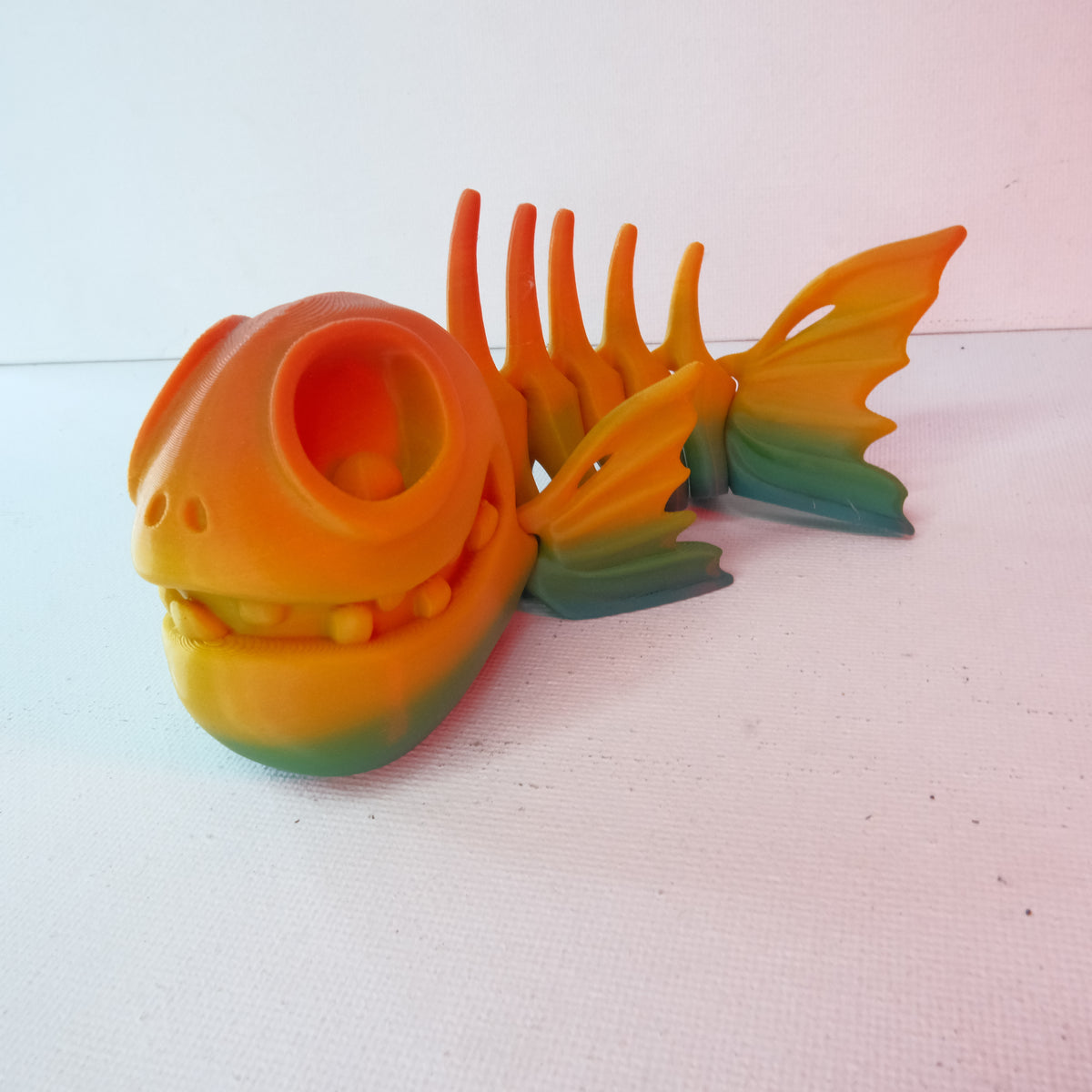 A colorful toy fish skeleton with articulated joints, featuring a large head and fins, smoothly blending orange and green shades.