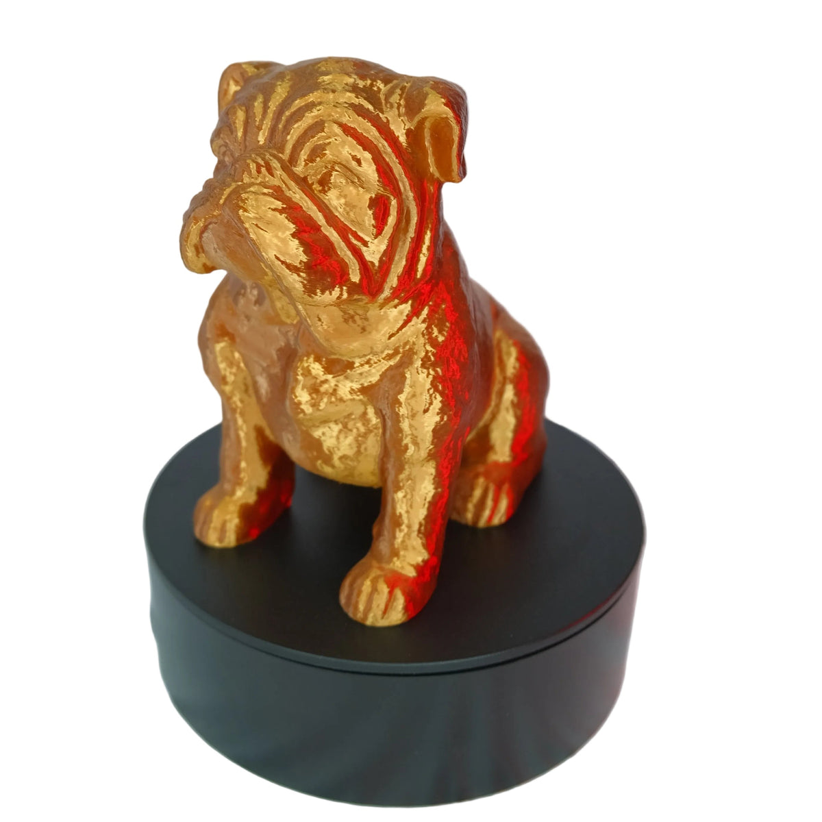 A glossy golden dog figurine posed sitting on a display base with a black surface against a white backdrop.