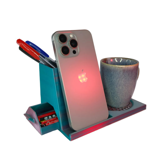 A sleek grey phone stand holding an iPhone with a glowing Apple logo, accompanied by a blue ceramic cup and colorful pens.