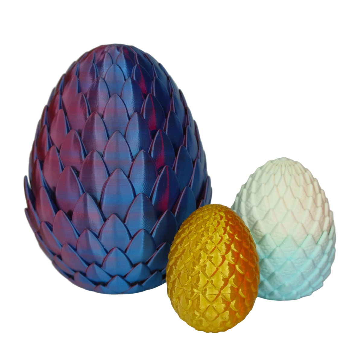 Three decorative eggs in vibrant colors: one large purple and blue egg with a textured surface, a medium yellow egg, and a small pale blue egg with a scaled pattern.
