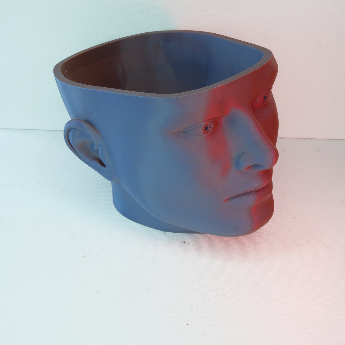 A blue novelty planter shaped like a human head, featuring a smooth surface and open top for planting.